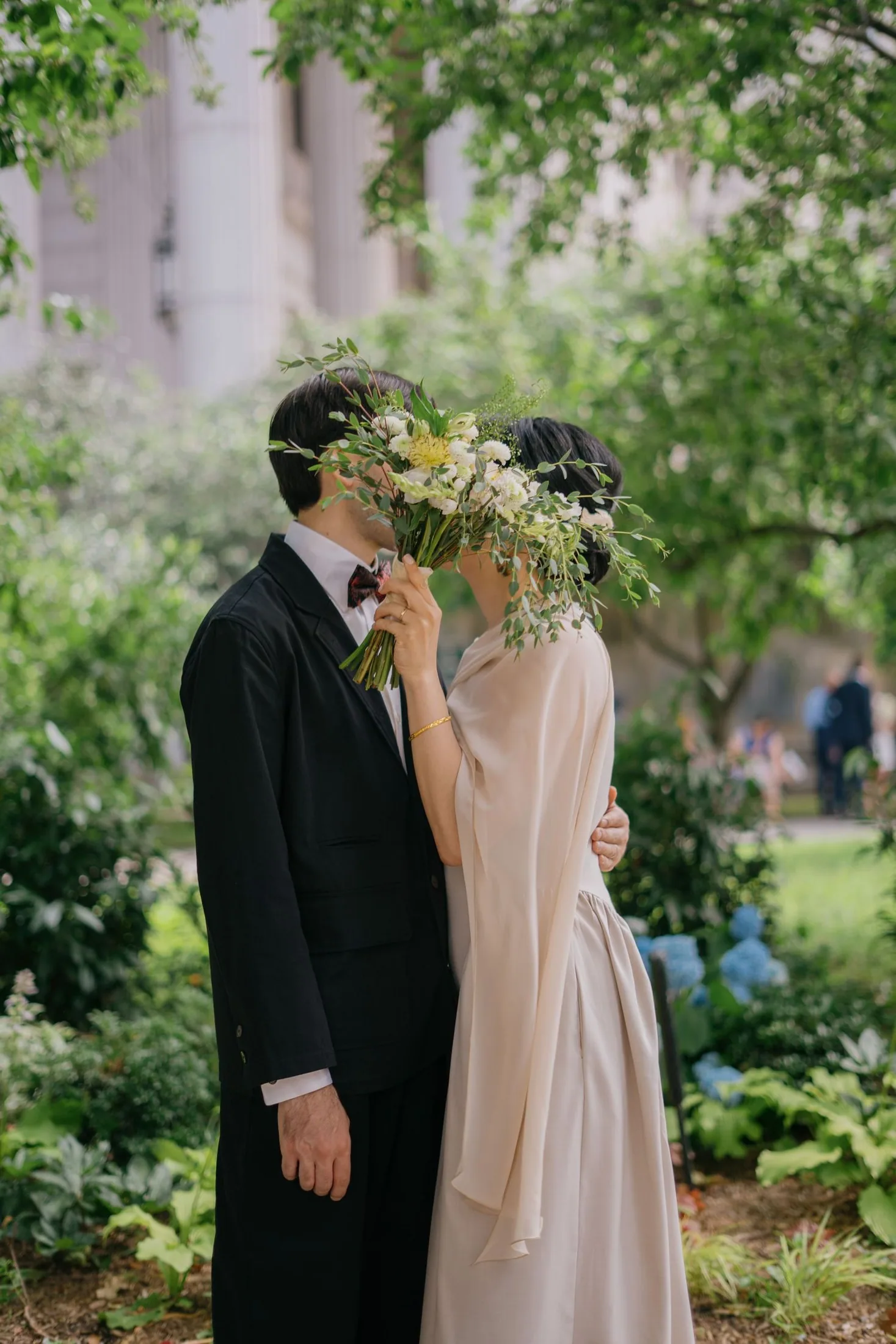 Newlyweds kissing beneath green garden branches